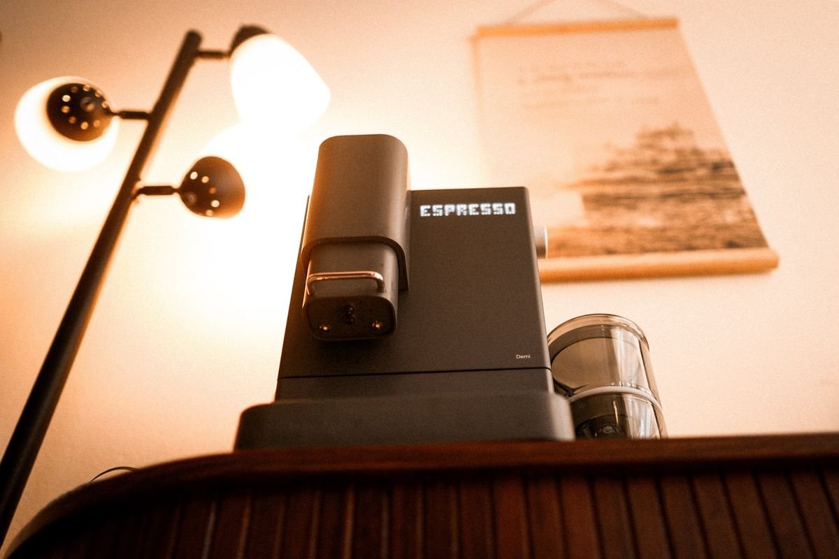Looking up at the Demi, its display reading ESPRESSO, with a floor lamp glowing behind