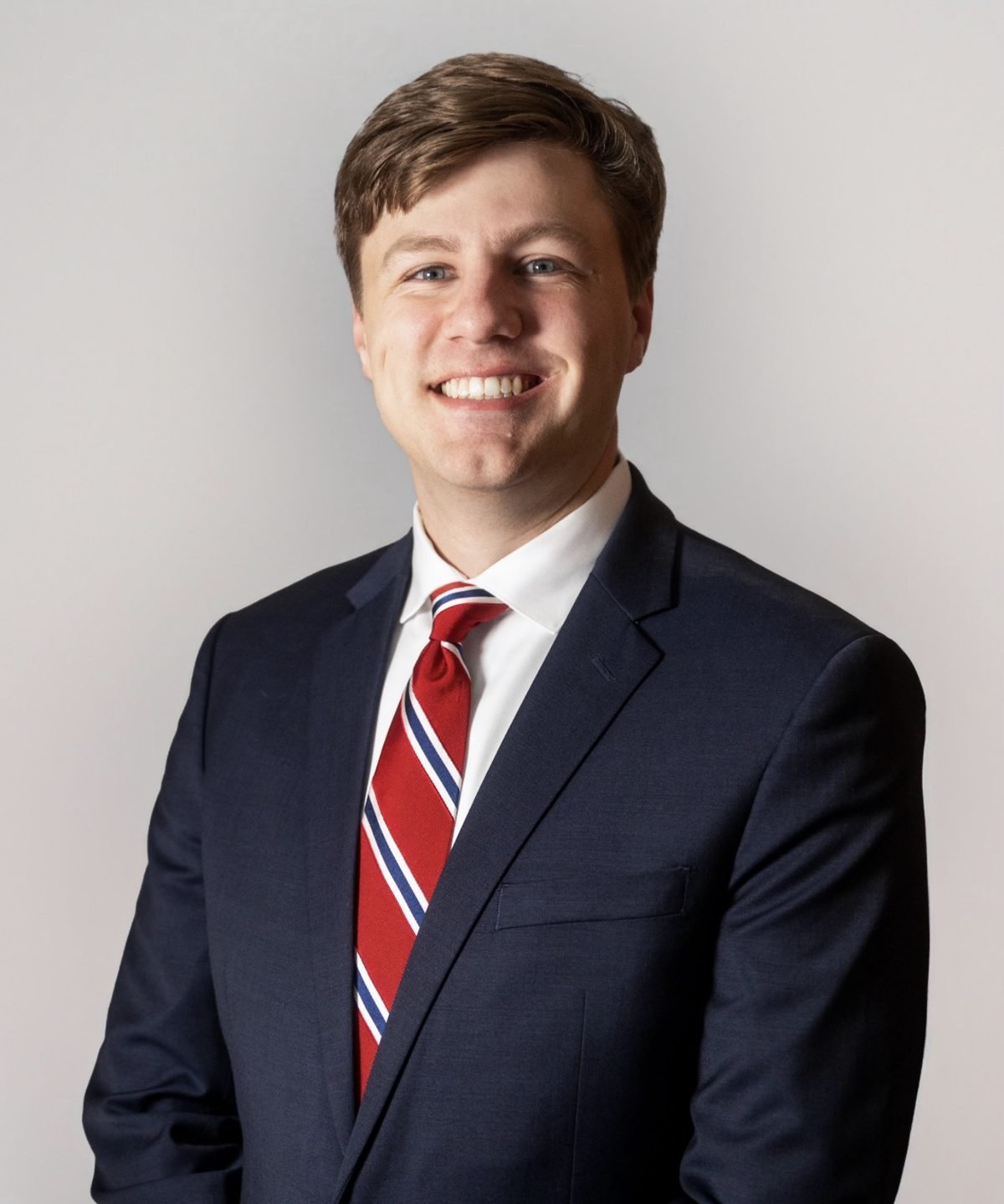 A smiling man in a navy suit and striped tie