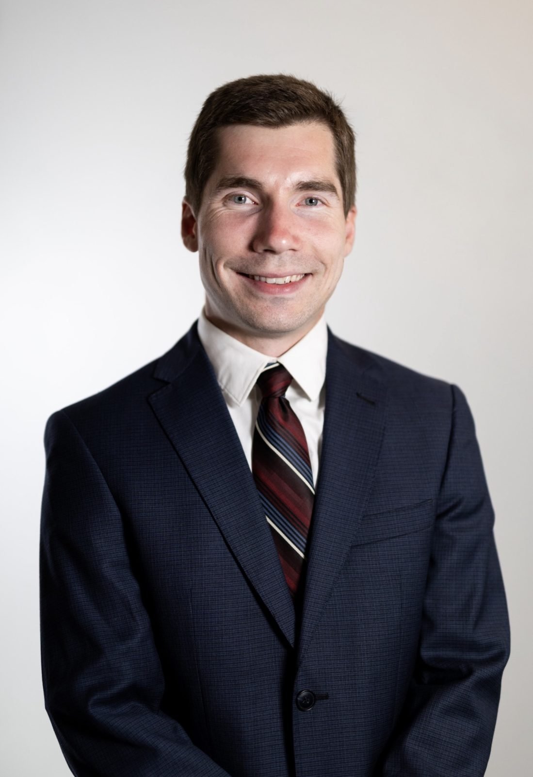 A smiling man in a navy suit on a light gray backdrop