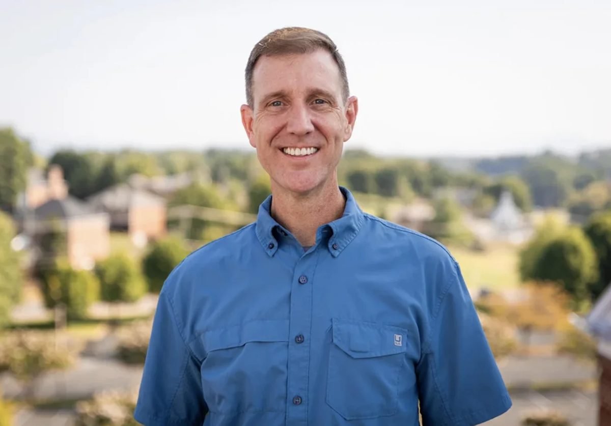A smiling man in a blue shirt, outdoors above a small town